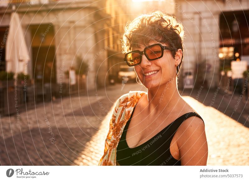 Young brunette on sunlit street at sunset woman smile style happy summer evening portrait madrid spain female young sundown cheerful positive sunglasses