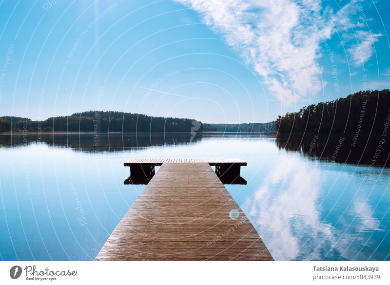 A wooden pier against the backdrop of a lake in the middle of the forest. Blue sky with clouds reflected in the water of Lake Baltieji Lakajai in Labanoras Regional Park