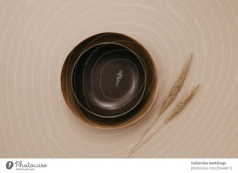 Brown and black plate on beige background with dried mini pampas grass. Flat lay, top view. Brown and natural color plates. Textured grainy pattern on the plates. Copy space on the table.