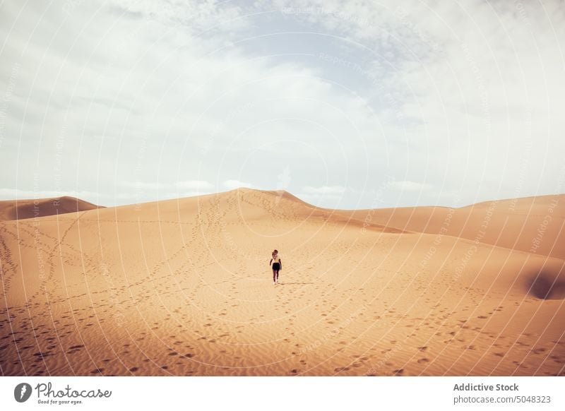 Anonymous woman walking on dune desert admire beach tourist explore blue sky sand maspalomas gran canaria canary islands spain weekend observe traveler vacation