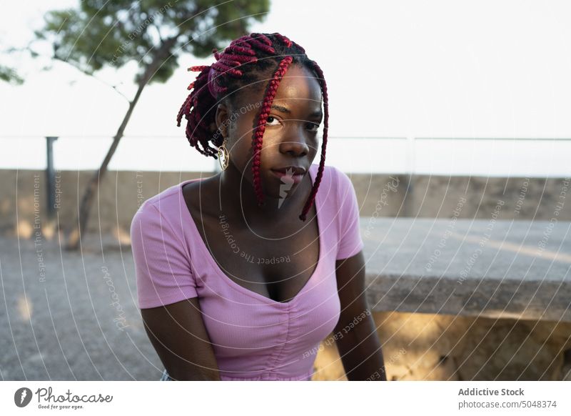 Black woman with dreadlocks relaxing near stone bench serious hairstyle vacation tourist pink confident trendy top female calm lady rest young casual freedom