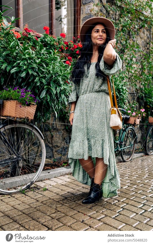 Happy female tourist walking on street woman romantic pavement explore smile stone wall bicycle building adult cheerful happy casual sunhat flower long hair