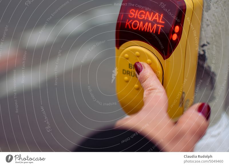 Woman's hand presses switch at demand light & writing 'Signal coming' lights up Demand traffic light Street crossing Pedestrian traffic light Please press