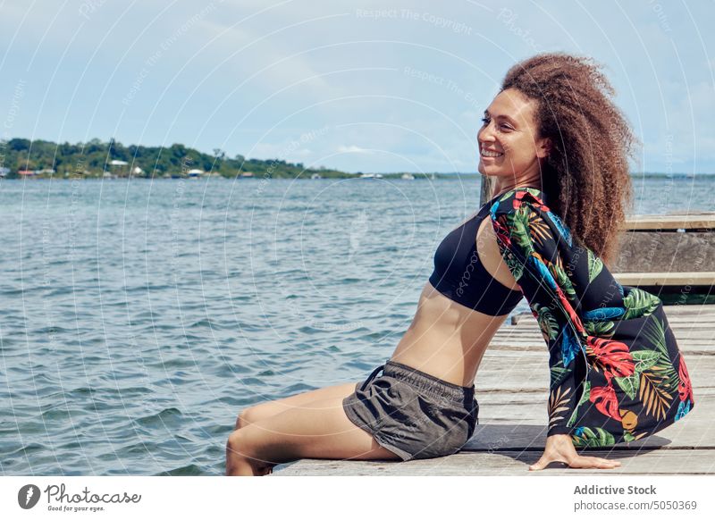 Relaxed smiling woman dangling legs in water from pier summer happy cheerful tropical rest carefree relax shabby peaceful serene sea nature calm curly hair