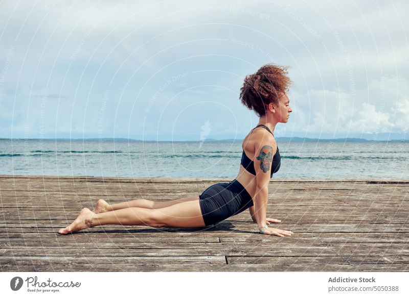 Calm ethnic woman in yoga pose on pier practice quay sea summer healthy bhujangasana cobra pose nature wellness harmony breath shore waterfront energy hispanic