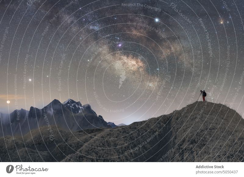 Traveler photographer standing on top of mountain in winter milky way man photography star night iceland vestrahorn photo camera tripod traveler dusk evening