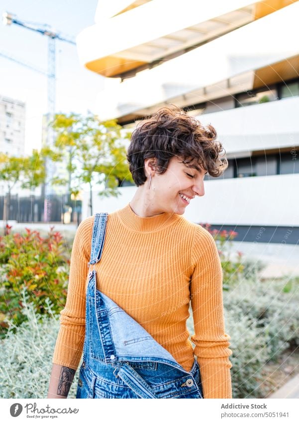 Cheerful woman standing in blooming shrubs against building summer cheerful flower smile blossom style eyes closed street summertime city enjoy jeans female