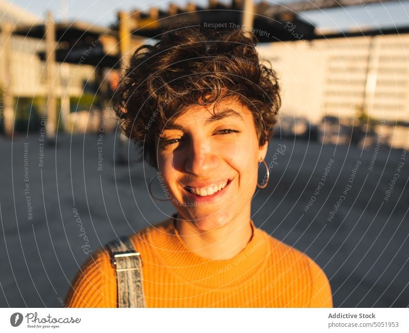 Happy woman standing on sunny street calm sunlight casual shadow city urban smile personality female alone short hair individuality building dark hair young