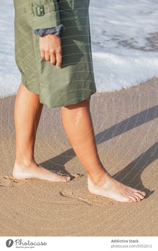 Crop barefoot woman walking along seaside water wave foam beach sand coast shore vacation nature female travel ocean holiday seashore wet splash tourism resort