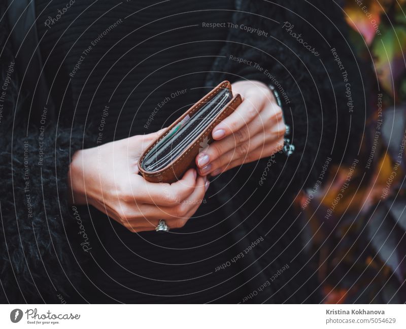 people, saving and finance concept - hands with cash money and wallet in autumn park. Close up hands of young woman with brown purse. female girl business