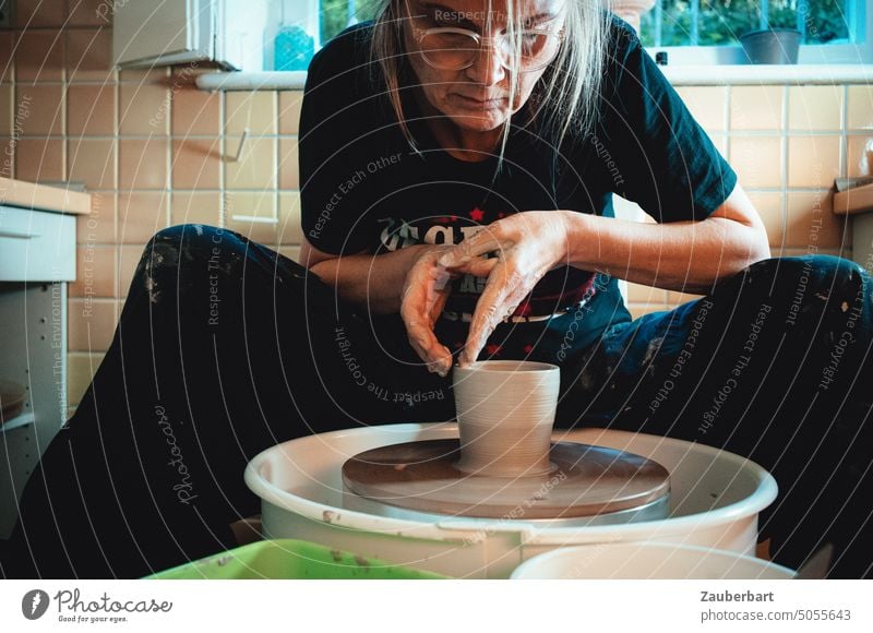 Pottery, woman in her pottery workshop concentrated forming a vessel from clay on the potter's wheel Do pottery Woman Tone Potter's wheel Raise walls