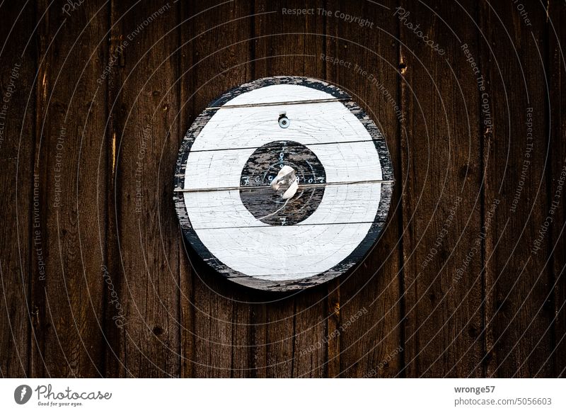 Older weathered target hangs on brown board wall Target Weathered old and weathered wooden disc wooden target protectionist society for the protection