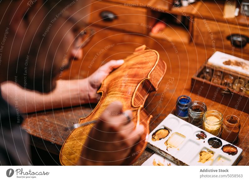 Focused luthier varnishing violin in workshop craftsman polish artisan master professional wooden instrument handicraft tool skill color manufacture woodwork