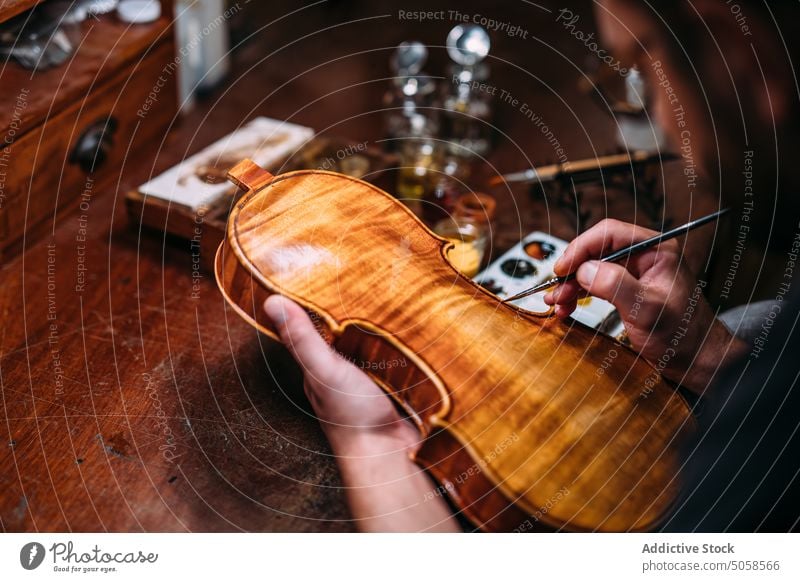 Focused luthier varnishing violin in workshop craftsman polish artisan master professional wooden instrument handicraft tool skill color manufacture woodwork