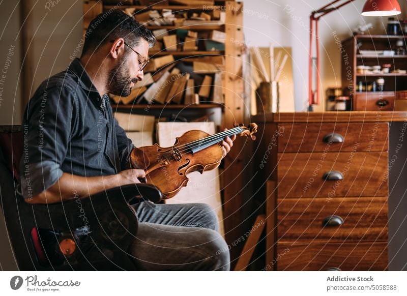 Male luthier with violin in workshop man instrument handicraft studio professional classic workplace craftsman check quality artisan manual master occupation