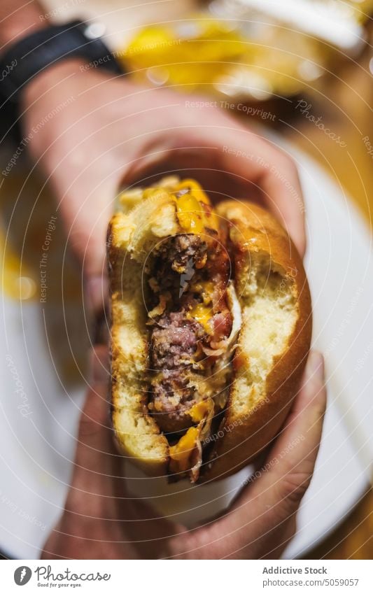 Unrecognizable person eating delicious burger hamburger fast food tasty appetizing scrumptious cheese plate meal lunch yummy patty dish table meat hungry