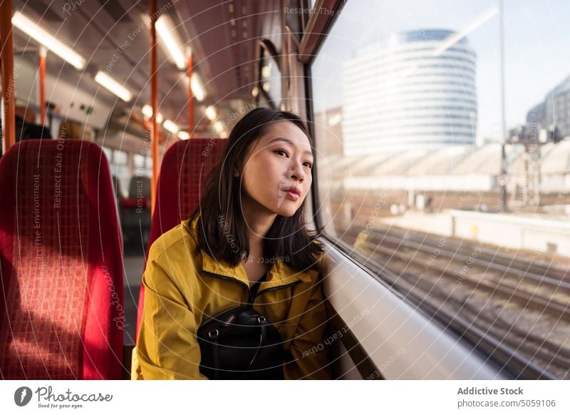 Asian woman riding train in city ride window passenger travel commute daytime public london england uk united kingdom female young transport trip railroad