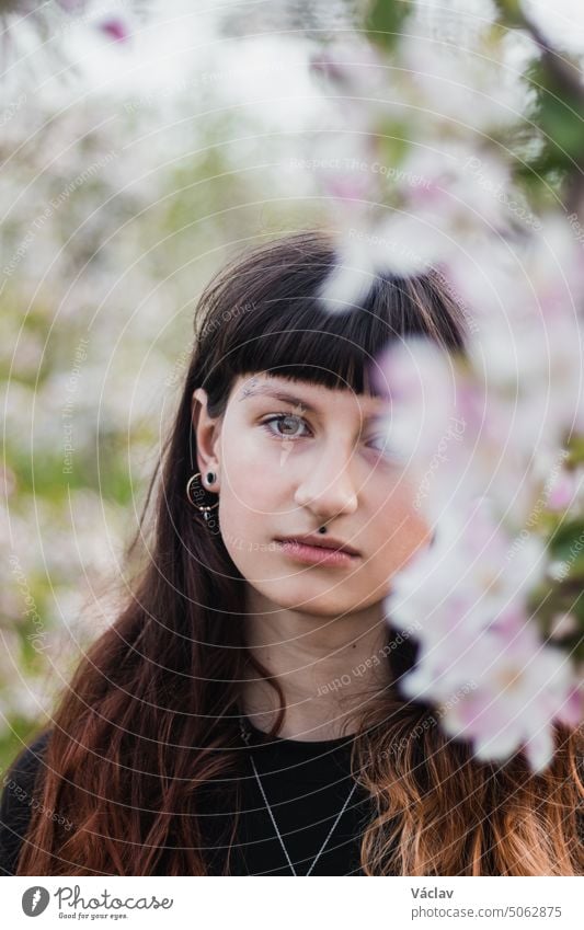 Candid portrait of a beautiful brown-haired woman with facial piercings in a blossoming apple orchard. Brown-eyed girl with cute face brown eyes relationship