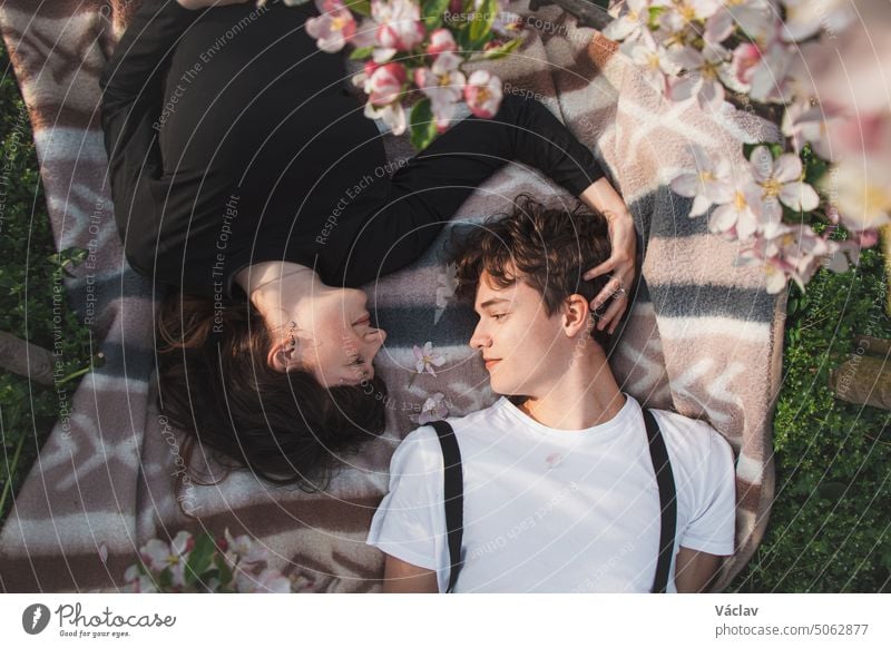 Young strong love between two young people lying on a blanket under apple trees. Candid portrait of a couple in casual clothes relationship girlfriend romance