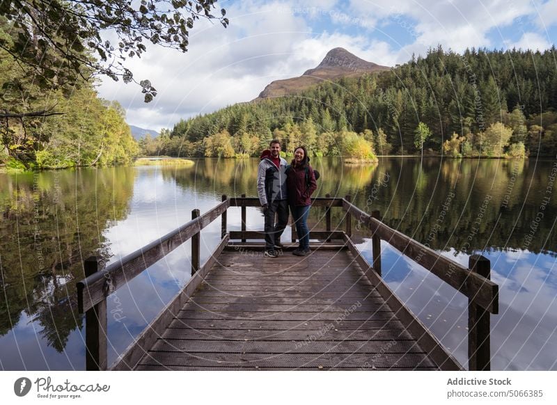 Diverse couple on quay near lake pier mountain forest hug together traveler smile happy glencoe lochan scotland uk united kingdom scottish highlands multiracial