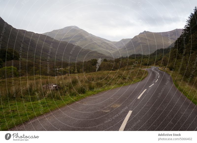 Curvy road in valley near mountains ridge curve gray cloudy sky countryside landscape scotland scottish highlands uk united kingdom asphalt overcast range