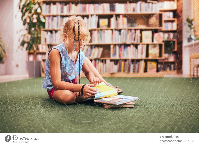 Schoolgirl reading and watching book in school library. Doing homework. Books on shelves in bookstore. Learning from books. Back to school back schoolgirl child