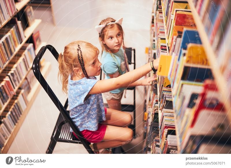 Schoolgirls looking for books in school library. Students choosing set books. Elementary education. Doing homework. Back to school back schoolgirl child reading