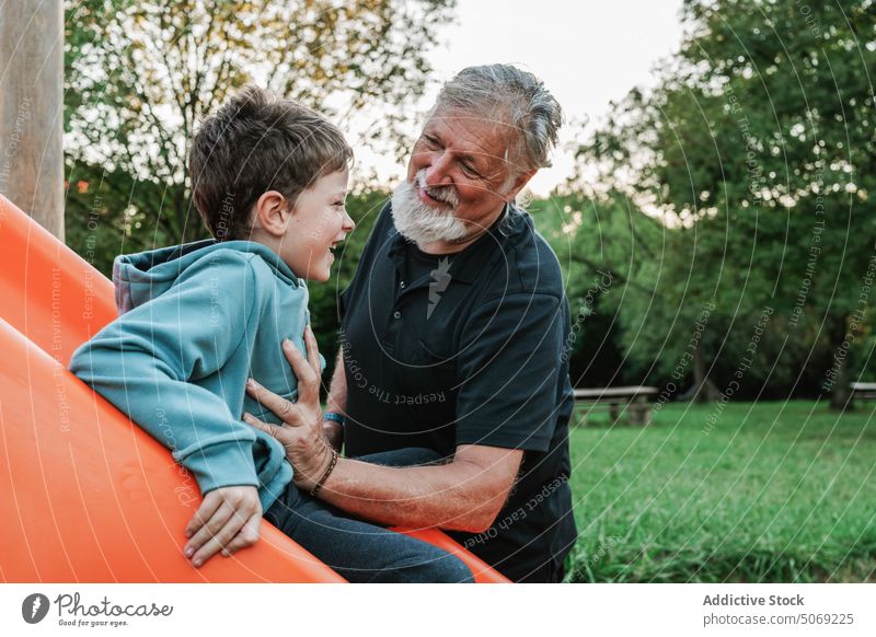 Grandson playing on slide near granddad grandfather grandson cheerful smile weekend summer together playground man boy preteen elderly senior aged park