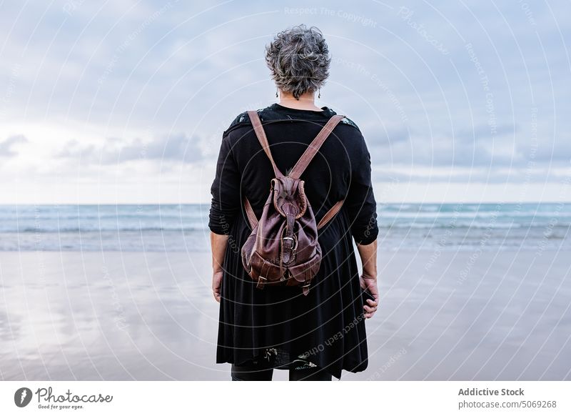 Senior woman standing on wet sand traveler sea beach resort weekend storm female elderly senior aged retire pensioner trip holiday wave tourism tourist water