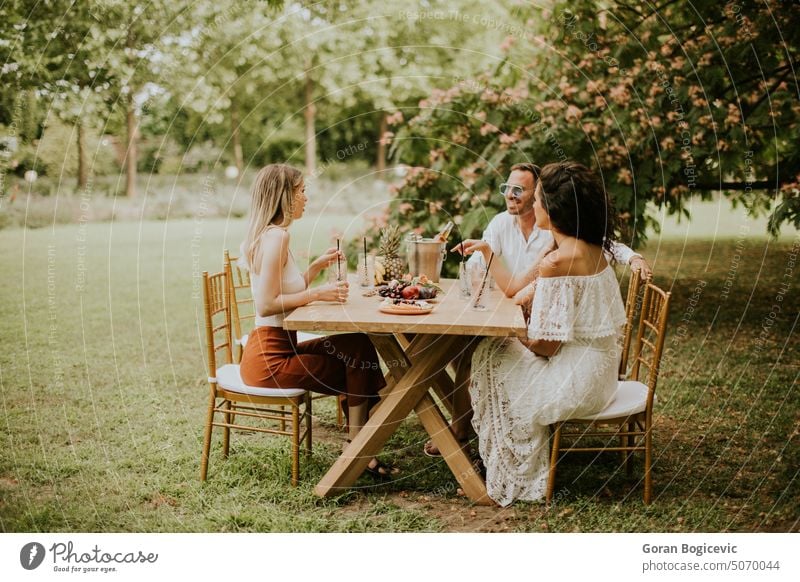 Group of happy young people drinkking fresh lemonade and eating fruits in the garden 20s party caucasian cheerful conversation enjoyment female food freshness