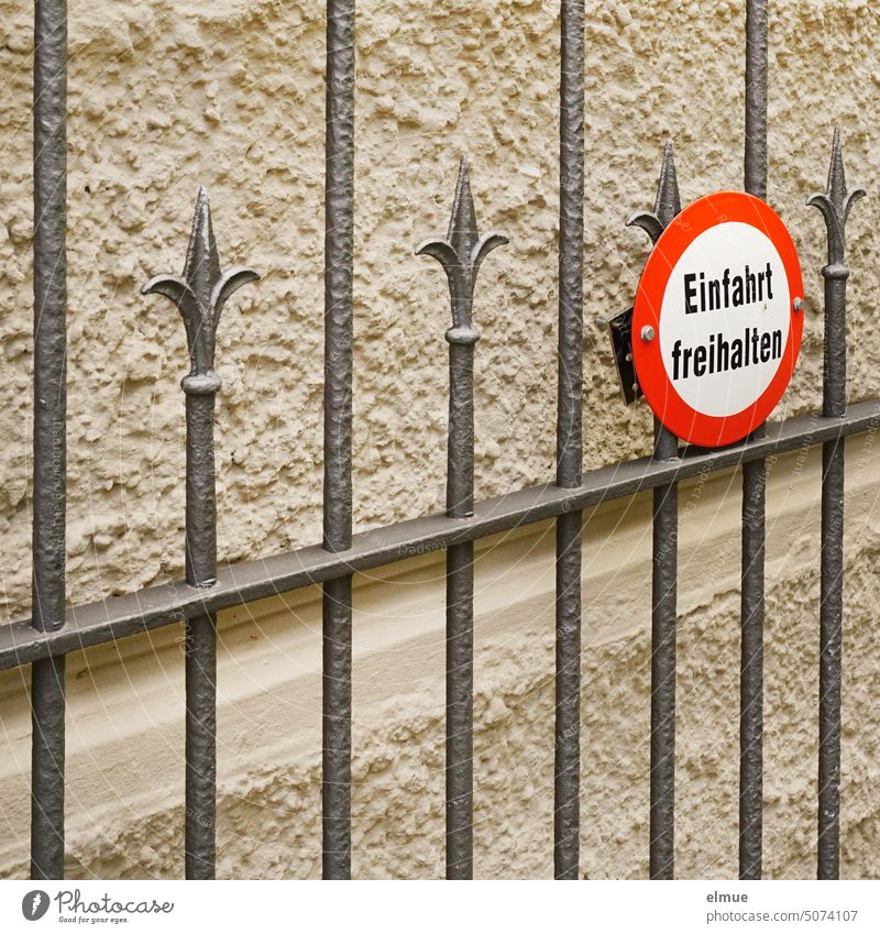 Metal gate on a rough plastered house wall and with a red bordered round sign - Keep driveway free -. metal gate Highway ramp (entrance) keep the driveway clear