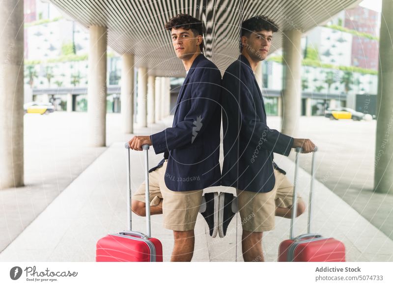 Young man with suitcase on street smile building airport traveler glass wall trip weekend male young smart casual baggage tourist style tourism daytime