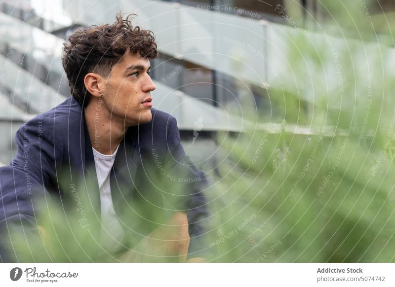 Young man behind bush on terrace street building summer urban modern daytime haunch male young smart casual dark hair foliage construction vegetate structure