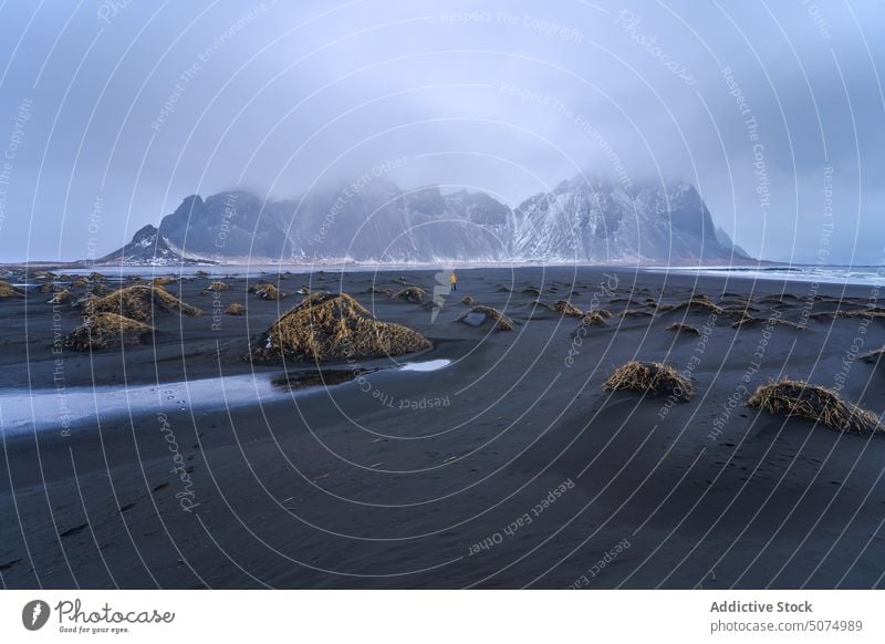 Unrecognizable traveler standing on sandy beach stockness shore wave sea vestrahorn mountain nature scenery iceland black tourist sky cloudy weather water coast