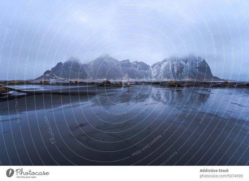 Unrecognizable traveler standing on sandy beach stockness shore wave sea vestrahorn mountain nature scenery iceland black tourist sky cloudy weather water coast