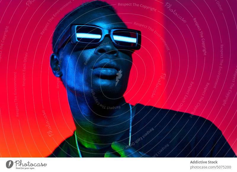 Eccentric black man in sunglasses and chain in neon illumination eccentric metaverse illuminate unemotional funky style glow fashion male cool trendy light