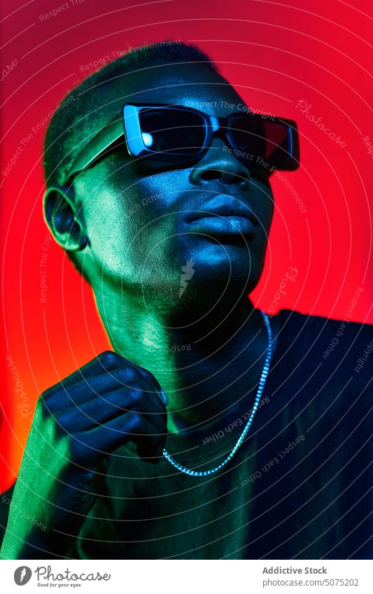 Eccentric black man in sunglasses and chain in neon illumination eccentric metaverse illuminate unemotional funky style glow fashion male cool trendy light