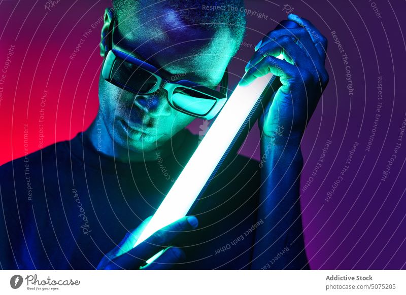 Extravagant black man in sunglasses with fluorescent lamp in hands extravagant metaverse reflect neon glow light chain male eccentric african american eyewear