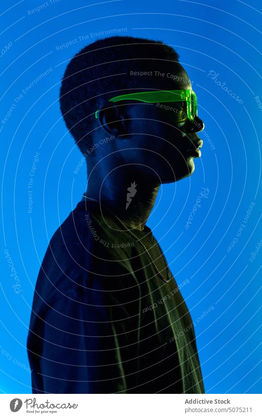 Unusual black man in sunglasses standing in neon light unusual metaverse ultraviolet strange bright glow male casual african american man colorful contemplate