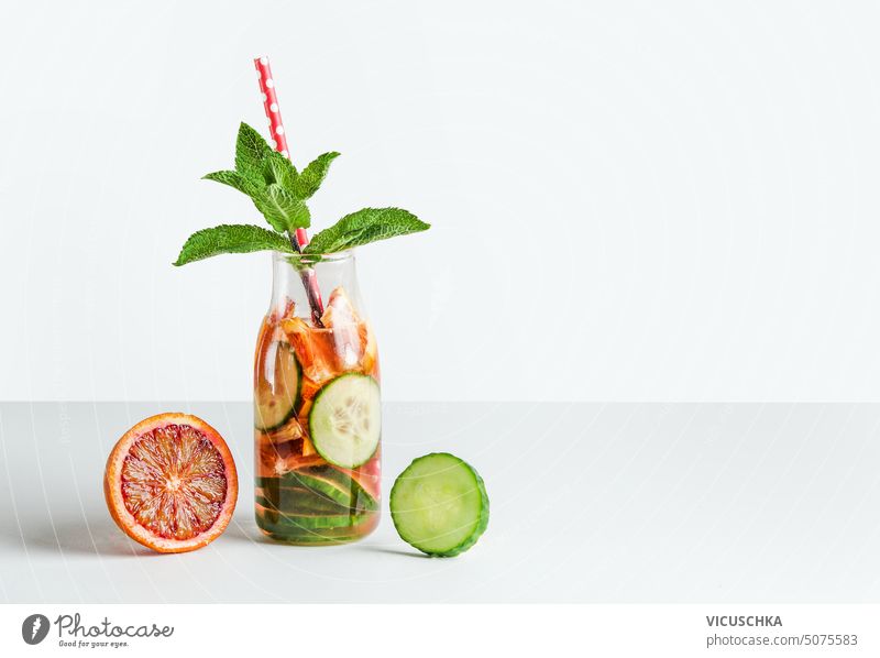 Infused watter with fruits and herbs in glass bottle with drinking straw on white table. Healthy drinks concept infused watter healthy drinks lemonade beverage