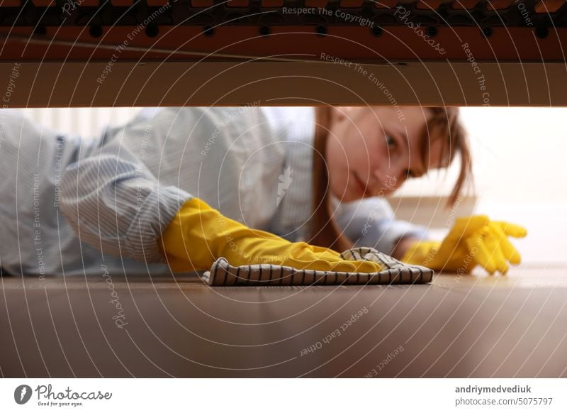 Cleaning and disinfection of surfaces. Woman with yellow rubber gloves and rag cleaning floor under bed. Beautiful woman cleaning house. housecleaning