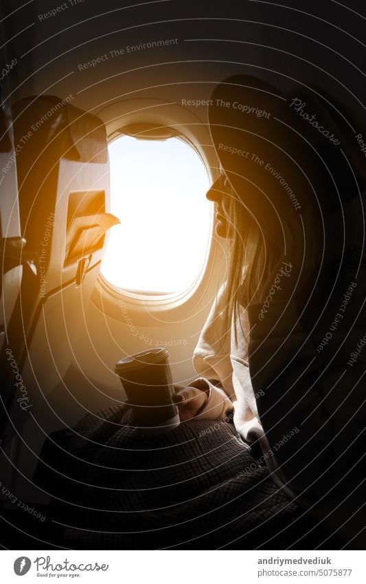 young woman in airplane. Female tourist sitting by the open airplane window at sunset. People traveling by airplane, transportation, vacation concept. female