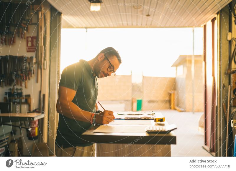 Focused craftsman counting expenses in joinery workshop artisan take note paper sheet write concentrate calculate finance industry table focus occupation job