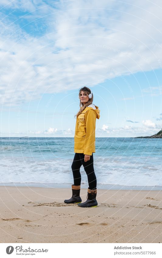 Woman in wireless headphones on the beach woman contemplate warm clothes listen song relax sandy coast wavy foam seashore female ondarreta beach cloudy sky