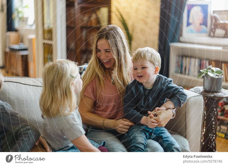 Mother with children sitting on sofa at home real life real people bonding family indoors quality time house parenting kids enjoyment day parenthood together