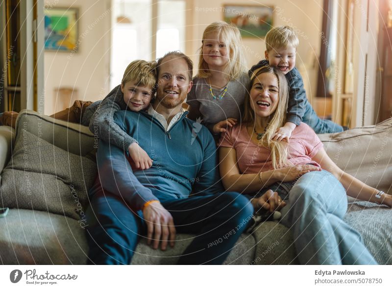 Happy young family sitting on sofa at home real life real people bonding indoors quality time house parenting kids enjoyment together fun happy togetherness