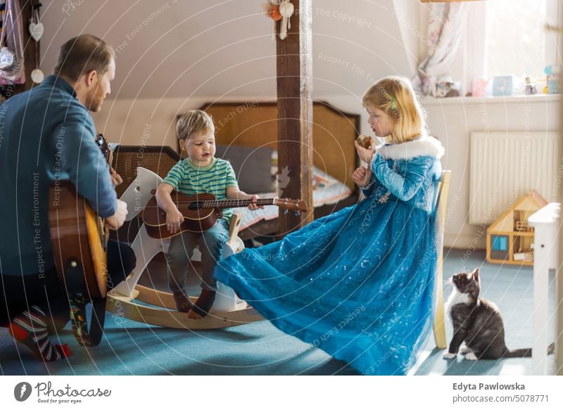 Dad teaching his kids how to play guitar modern manhood genderblend real life real people bonding family indoors quality time house parenting enjoyment together