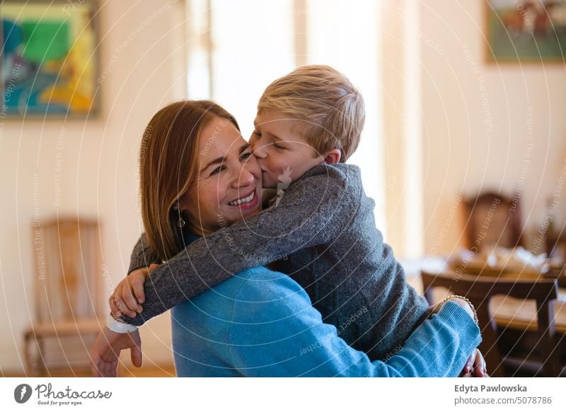 Son hugging his mom and kissing her on the cheek real life real people bonding family indoors quality time house parenting kids enjoyment day parenthood