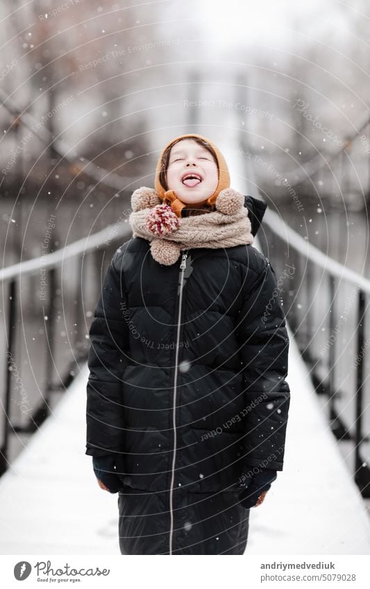 Funny little girl catches snowflakes in a beautiful winter park during a snowfall. Cute baby is playing in the snow. Winter activities for children. the winter holidays. happy childhood.