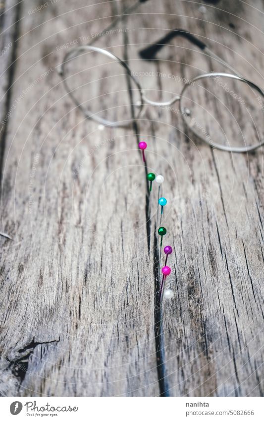 Line of colorful pins in a wooden table and a glasses rustic background texture vertical thread multi colored old aged vintage detail sewing couture surface